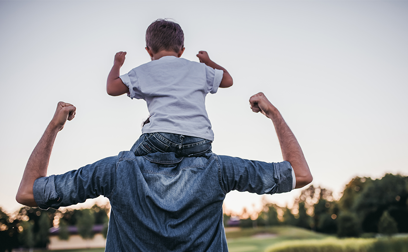 son on fathers shoulders showing off muscles