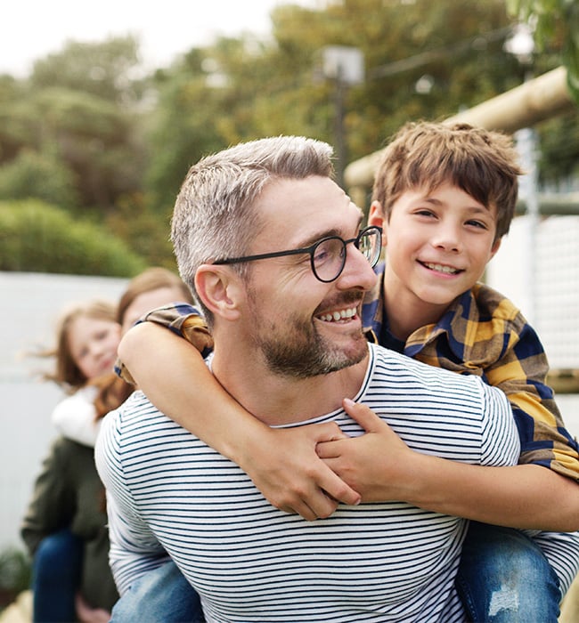 father wearing glasses with son on his back