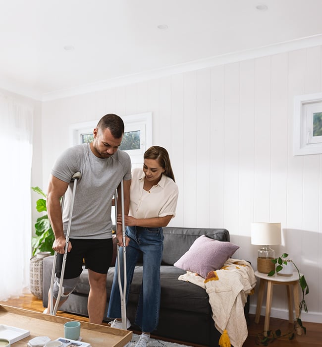 man on crutches with support worker at home